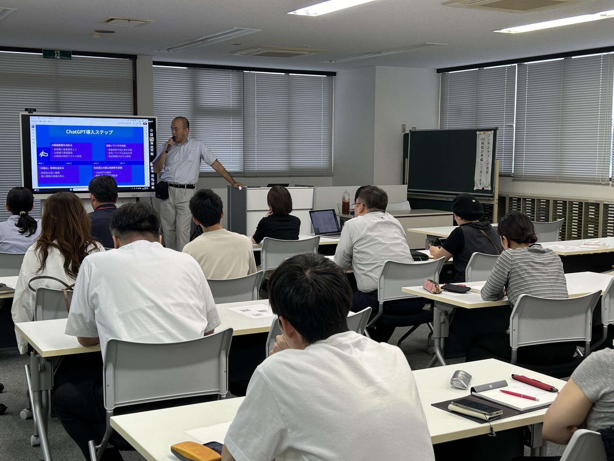 ChatGPT導入ステップを画面に示し、マイクを持って受講者へ説明する株式会社はちえん。坂田誠の過去の生成AI研修風景